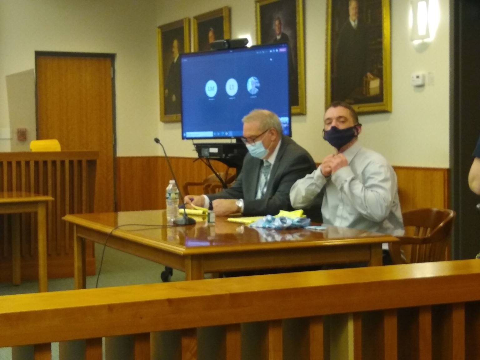 A couple of men sitting at a table with a projector screen behind them

Description automatically generated with low confidence