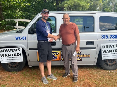 Two men shaking hands in front of a white van

Description automatically generated