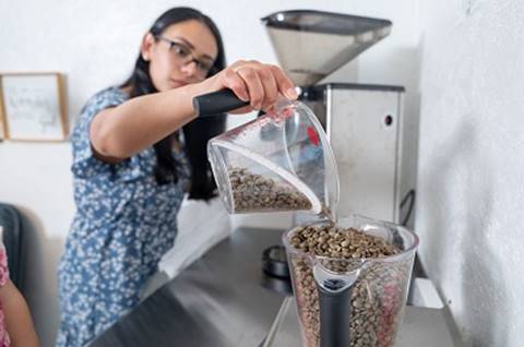 A person pouring coffee beans into a blender

Description automatically generated