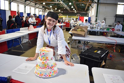 A person in a white coat and hat leaning on a cake

Description automatically generated