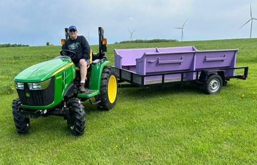 A person on a tractor pulling a purple trailer

Description automatically generated
