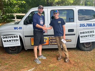 A person and child shaking hands in front of a van

Description automatically generated