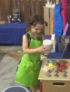 A young child wearing green apron

Description automatically generated